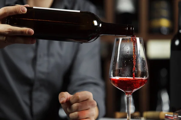 Close up tiro de sommelier derramando vinho tinto de garrafa em vidro — Fotografia de Stock