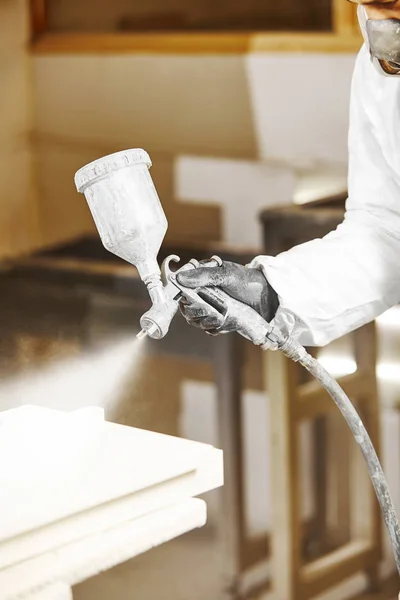 Close-up vertical image of man spraying with gun to the wood.