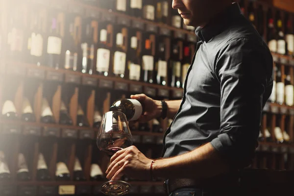 Manliga sommelier hälla rött vin i långhärdade wineglasses. Servitör med en flaska alkohol dryck. — Stockfoto