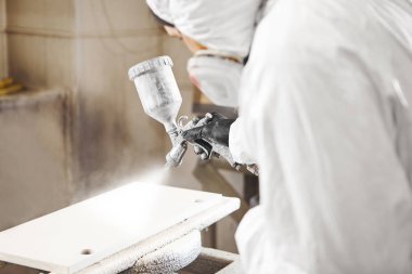 Boyalı sprey tabancayla çalışan, oduna havasız sprey sıkan bir adam.