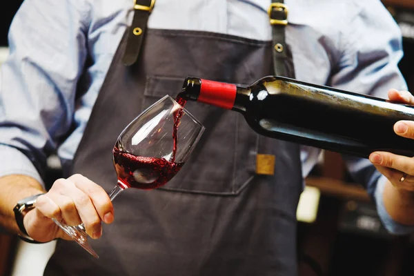 Férfi sommelier vörösbort öntve hosszú szárú borosüvegekbe. — Stock Fotó