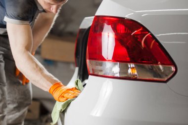 Adam elinde mikrofiber tutar ve beyaz araç parlatır. Araba detaylandırma.