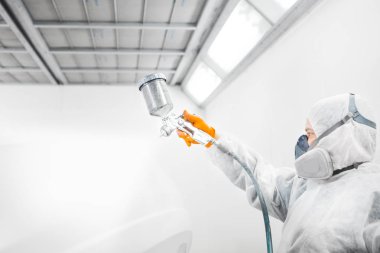 Profesyonel erkek araba boyacısı garajda boya yapıyor. Adam sprey tabancayla çalışıyor..