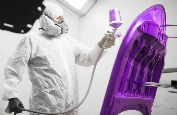 Trabajador pinta capucha de auto en color violeta con pistola pulverizadora. Coche blanco en una cámara de pintura durante los trabajos de reparación . — Foto de Stock