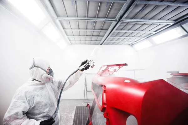 Car painter sprays varnish in paint booth.