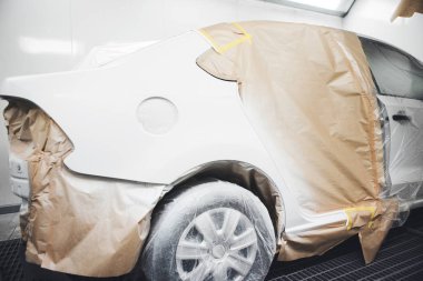 Vücut tamir atölyesindeki sprey boya kabinine beyaz araba cesedi boyamak, elementler koruyucu kağıtlarla kaplıdır..