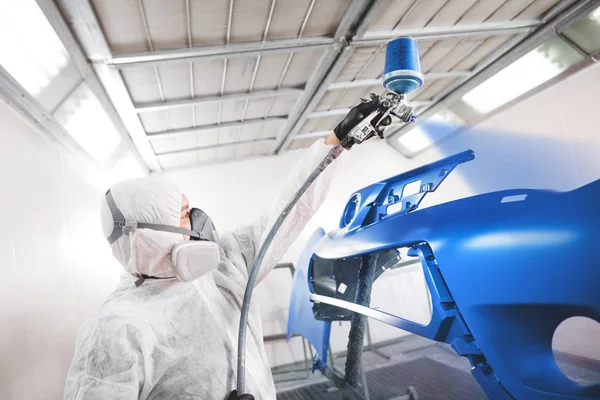 Male worker in protective clothes and mask painting car bumper using spray paint. — Stock Photo, Image