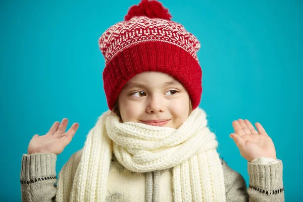 Frente close-up retrato de menina em chapéu de inverno vermelho e cachecol branco no fundo azul, levantou as mãos para cima, olha os olhos lateralmente, tem um rosto bonito e expressão sincera . — Fotografia de Stock