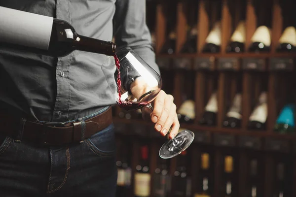 Αρσενικός οινομπόχος που ρίχνει κόκκινο κρασί σε μακρύ κοτσαδίδιο, με κοντινό πλάνο. Σερβιτόρε με μπουκάλι αλκοολούχο ρόφημα. — Φωτογραφία Αρχείου