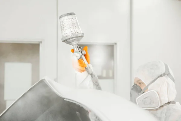 Pintor de corpo com pistola de ar pulverizando tinta branca em um automóvel na sala de pintura de serviço de manutenção de carro. — Fotografia de Stock