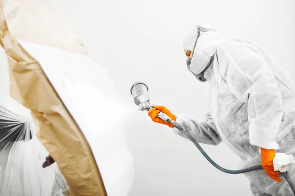 Maschio lavoratore in abiti protettivi e maschera pittura auto utilizzando vernice spray . — Foto Stock