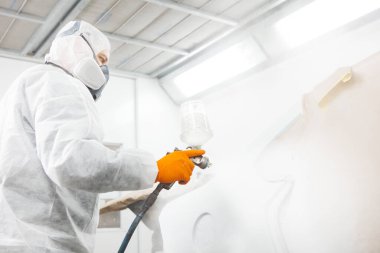 İşçi otomatik elementleri sprey tabancayla boyuyor. Tamir sırasında boya odasında beyaz bir araba..