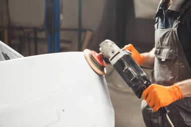 Araba cilalamak. Yörünge parlatıcısı olan bir işçi tırmalanarak kaportayı düzeltiyor..