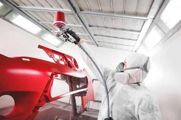Auto mecánico trabajador pintura coche elemento con pistola de pulverización en una cámara de pintura durante los trabajos de reparación . — Foto de Stock