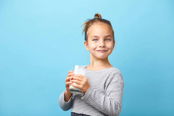 Belle petite fille avec verre de lait, se tient sur bleu isolé. — Photo