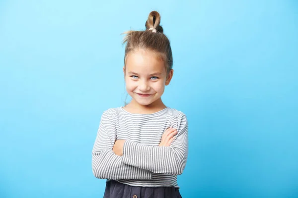 Menina bonita sorrindo, cruzou as mãos, tem uma expressão positiva, de pé sobre azul isolado . — Fotografia de Stock