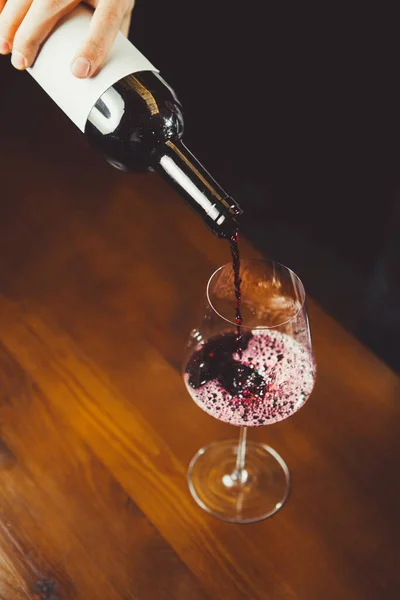 Close up tiro de sommelier derramando vinho tinto de garrafa em vidro — Fotografia de Stock