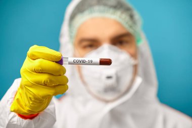 Koruyucu giysili doktor Coronavirus 'un kan örneği için tıbbi tüpü tutuyor. Corona virüsü salgını.