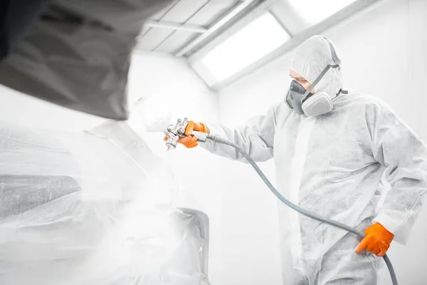 Trabajador masculino con máscara y ropa protectora pintando coche usando compresor de aerosol. —  Fotos de Stock