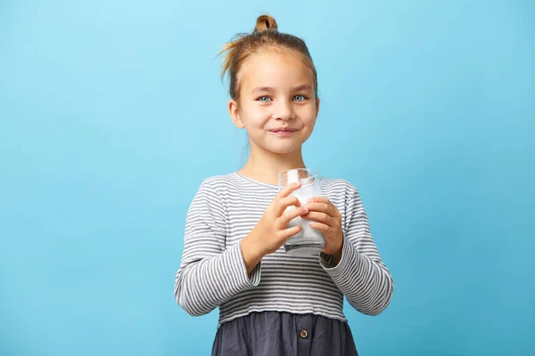 Portrait d'une enfant souriante tenant un verre de lait sur un isolant bleu. — Photo