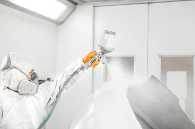 Profesyonel erkek araba boyacısı garajda boya yapıyor. Adam sprey tabancayla çalışıyor..