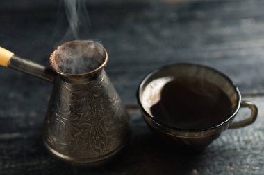 Jezve 'de koyu bir arka planda taze demlenmiş kahve. İçkiden çıkan sıcak buhar.