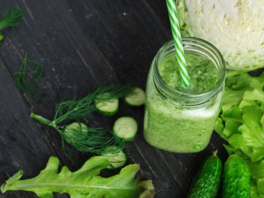 Yeşil salatalık suyu. İçi malzemelerle dolu, ahşap bir masada bir bardakta kilo vermek için.