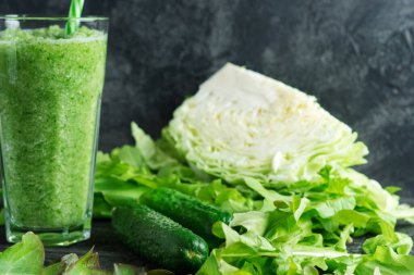 Yeşil salatalık suyu. İçi malzemelerle dolu, ahşap bir masada bir bardakta kilo vermek için.