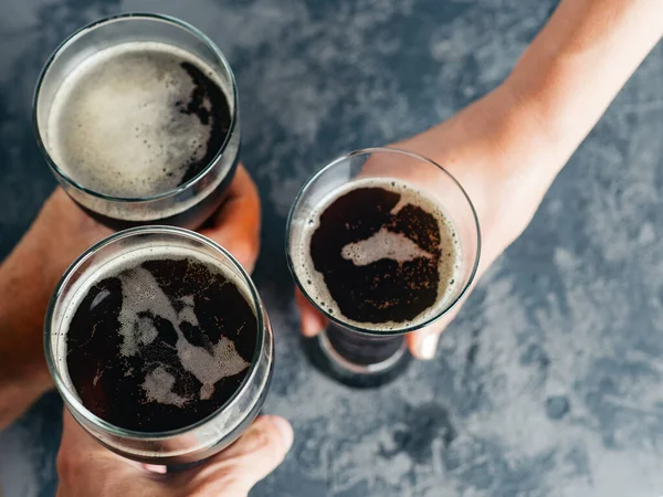 Glasses of dark beer . Friends make toast at the bar .