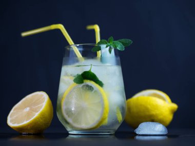 Bir bardak ferahlatıcı yaz mojito limonatası limon, nane ve ezilmiş buz yakın plan, sarı pipetler.