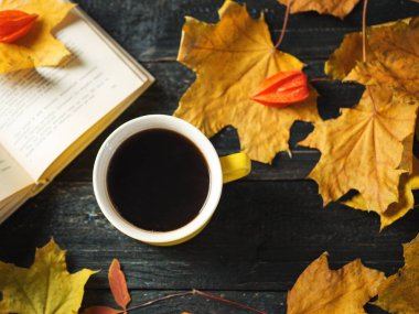 Sarı kahve fincanı ve kitap koyu ahşap bir masa üzerinde sonbahar eşarbı ve yaprakları ile