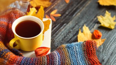 Sonbahar rahatlığı. Renkli bir atkıyla bir kupa sıcak kahve ahşap arka planda renkli sonbahar yapraklarıyla fotokopi alanı