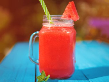 Mavi bir masada cam bardakta karpuz limonatası.