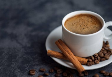 Tarçınlı beyaz espresso kahve fincanı ve koyu beton arka planda kahve çekirdekleri.