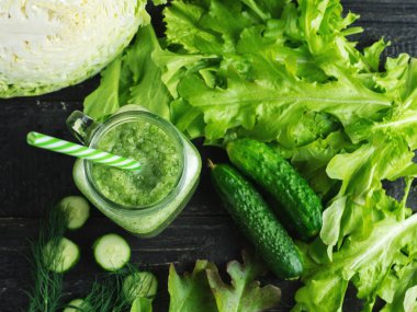 Koyu ahşap bir masa üzerindeki malzemelerle cam bir kavanozda yeşil smoothie yakın çekim