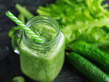 Koyu ahşap bir masa üzerindeki malzemelerle cam bir kavanozda yeşil smoothie yakın çekim