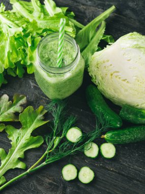 Koyu ahşap bir masa üzerindeki malzemelerle cam bir kavanozda yeşil smoothie yakın çekim