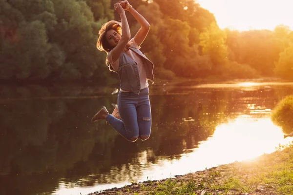 A young woman jumps with happiness at sunset. at sunset by the river