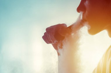 Adam arka planda elektronik sigara içiyor.