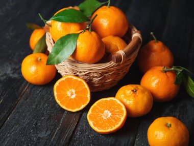 Sulu, parlak, olgun mandalinalar. Ahşap sepette, karanlık arka planda.