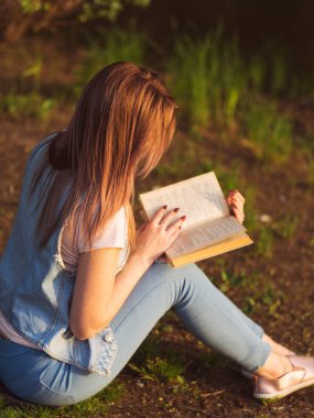 Gün batımında parkta kitap okuyan genç bir kadın.