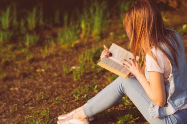 Gün batımında parkta kitap okuyan genç bir kadın.