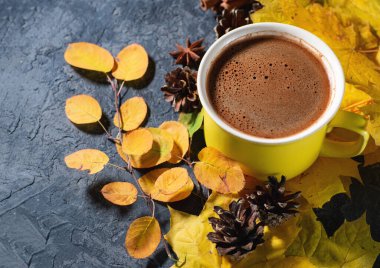 Sarı kahve fincanı, sonbahar yaprakları, tarçın ve kopyasıyla birlikte koyu taş masanın üzerinde.