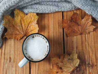Kuru sonbahar yaprakları ve sıcak bir eşarpla ahşap bir masada tarçınlı kahve kupası kapuçinosu.