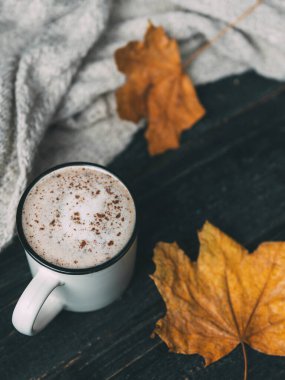 Kuru sonbahar yaprakları ve sıcak bir eşarpla ahşap bir masada tarçınlı kahve kupası kapuçinosu.