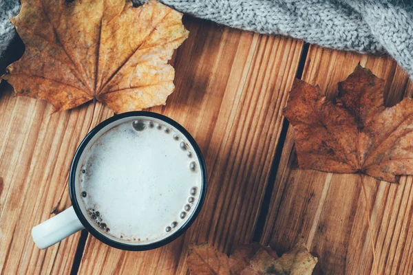 Kuru sonbahar yaprakları ve sıcak bir eşarpla ahşap bir masada tarçınlı kahve kupası kapuçinosu.