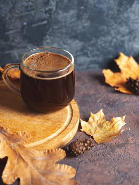 Masanın üzerinde cam kahve fincanı ve kuru sonbahar yaprakları var. Ev konforu