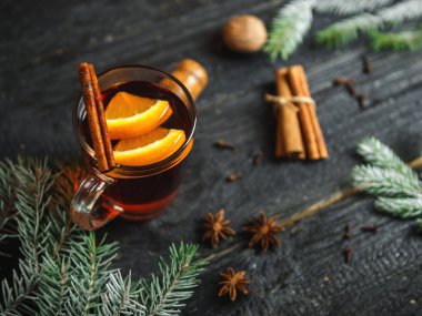 Sıcak kış içeceği koyu ahşap bir masada baharat ve Noel ağacı dallarıyla sulandırılmış şarap.