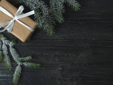 Kraft kağıdında hediye kutusu ve siyah tahta masada beyaz kurdele ve Noel ağacı dalları.