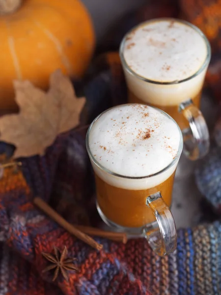 Pumpkin coffee latte. Autumn background with dry leaves and warm bright scarf . Home comfort hygge
